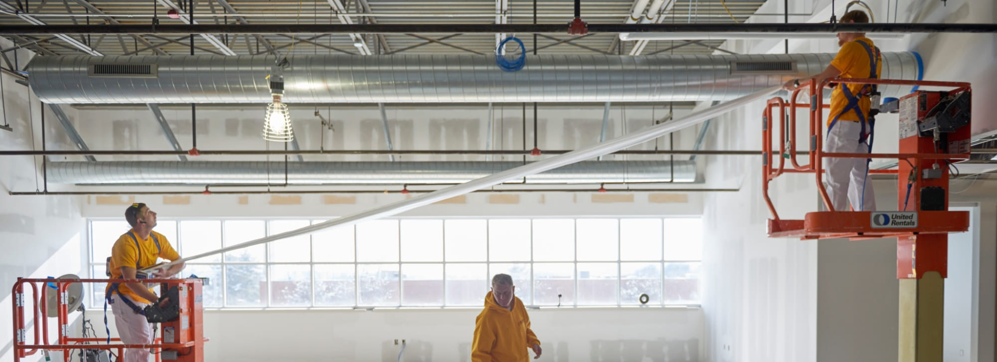 Three CertaPro painters spraying the ceiling of an open commercial interior from lifts